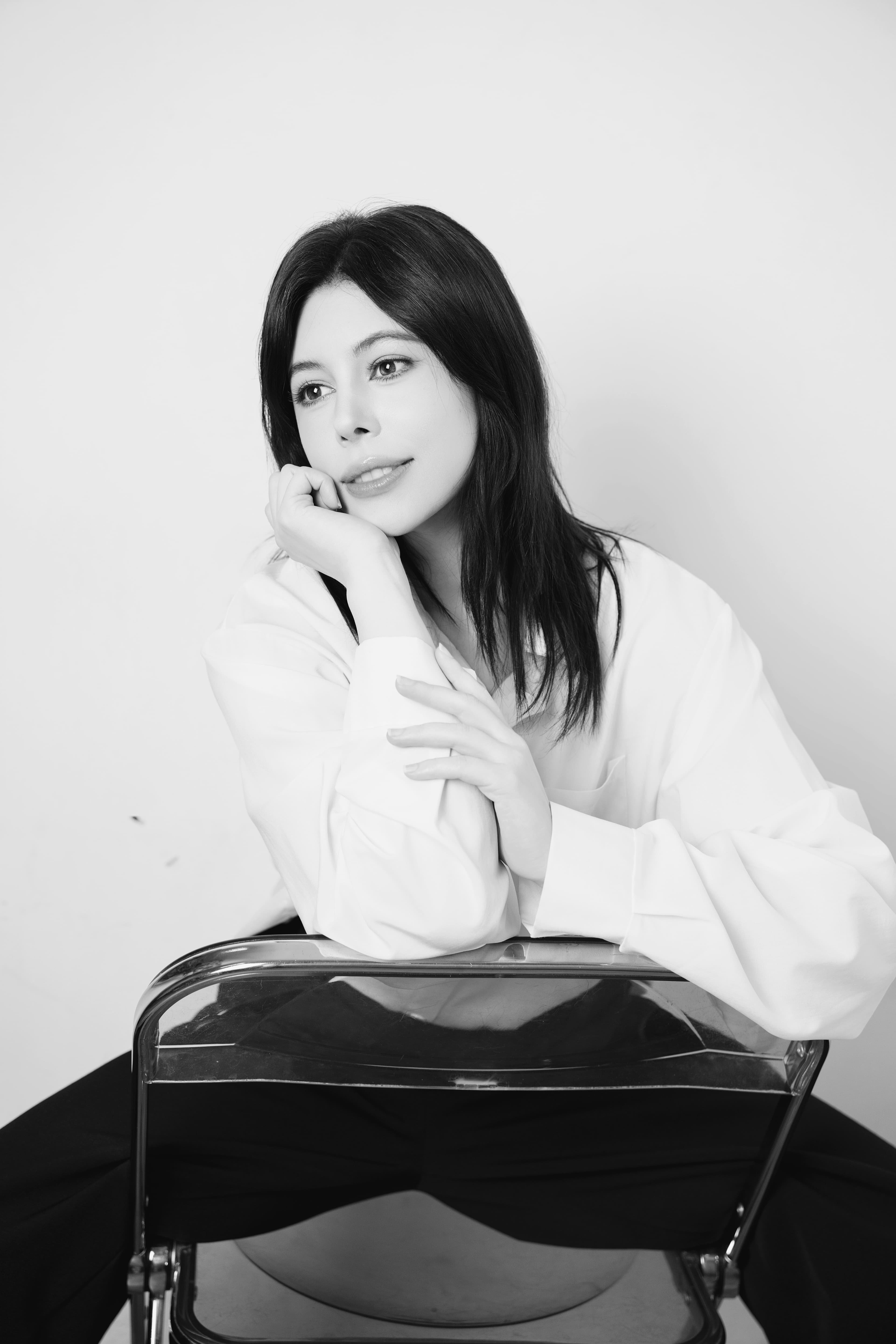 Black and white portrait of a woman sitting backwards on a chair, resting her chin.