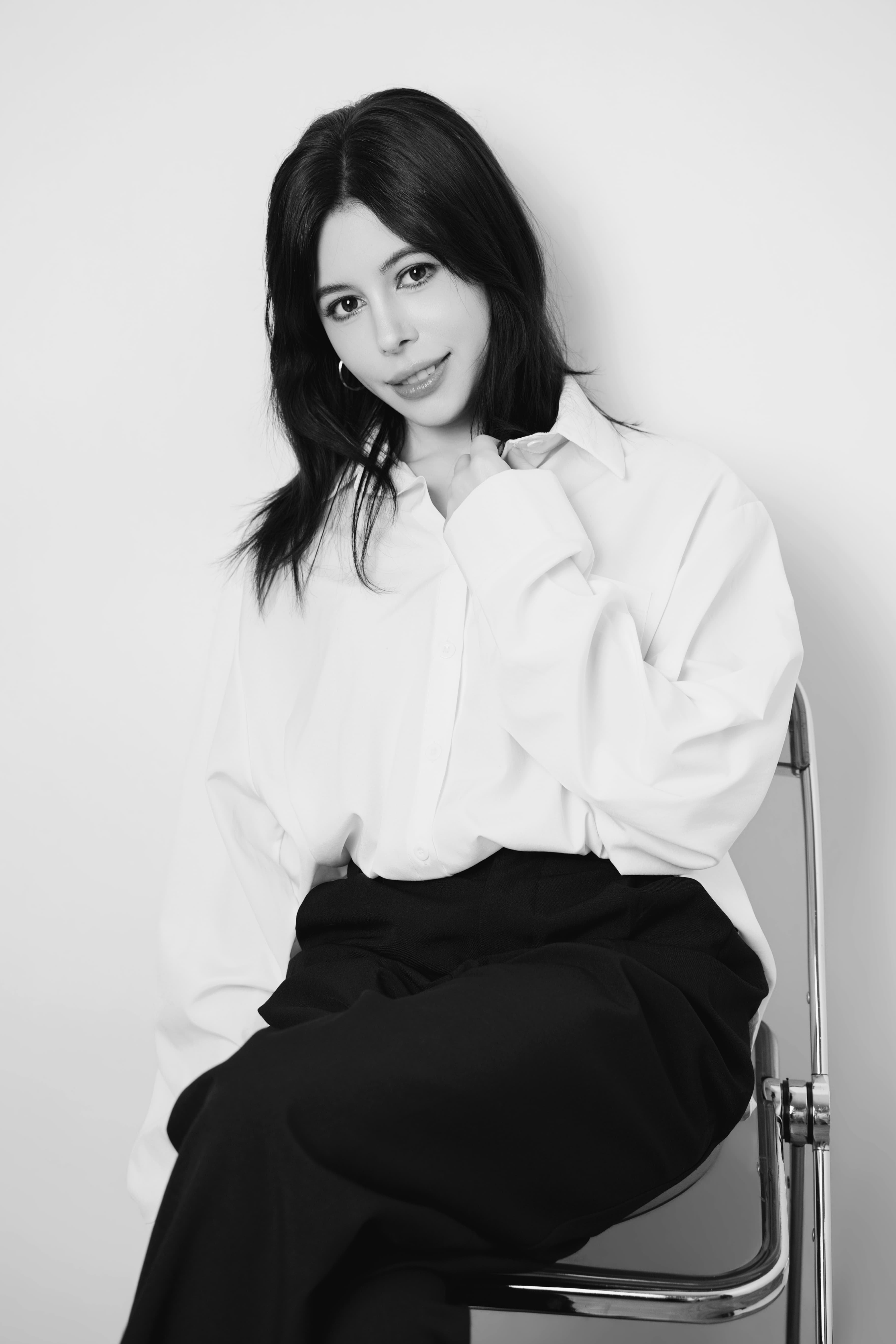 Black and white portrait of a woman in a white shirt and dark trousers, sitting.