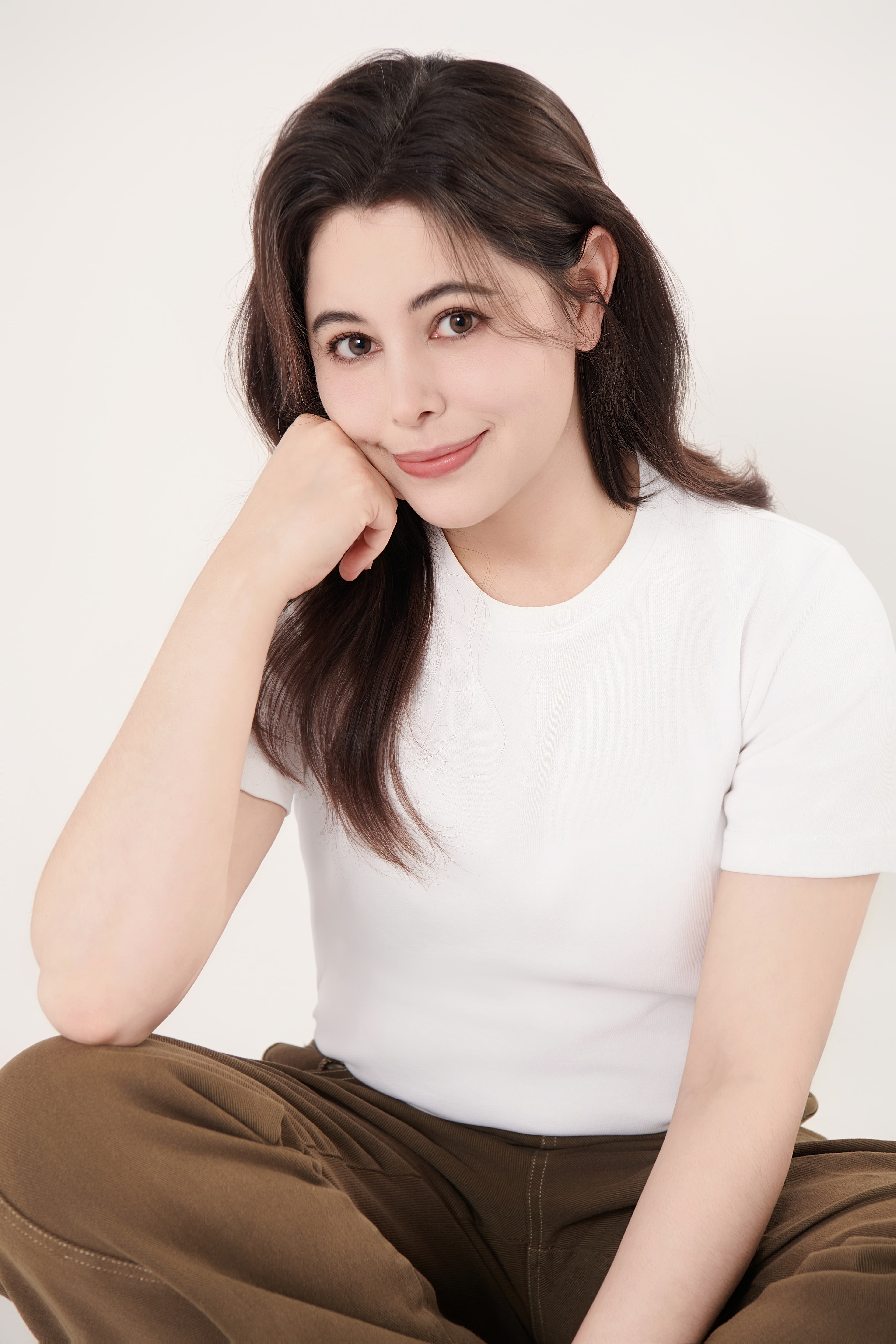 Smiling woman with dark hair in a white t-shirt, leaning her chin on her hand.